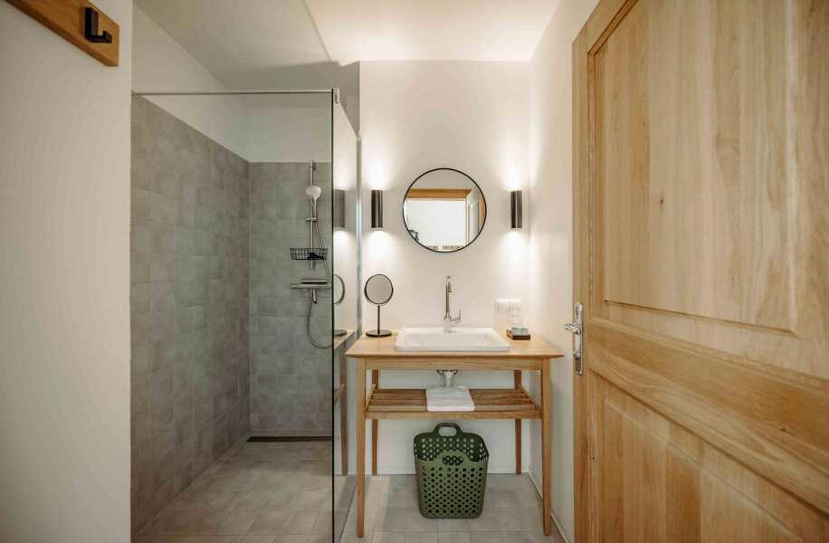 Modern bathroom with a wooden door, glass shower, round mirror, and wooden sink counter.