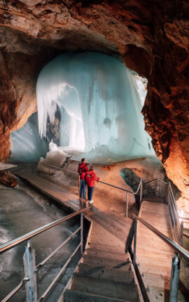 Ein Paar erkundet eine beeindruckende Eisformation in einer Höhle mit hölzernen Gehwegen und Geländern.