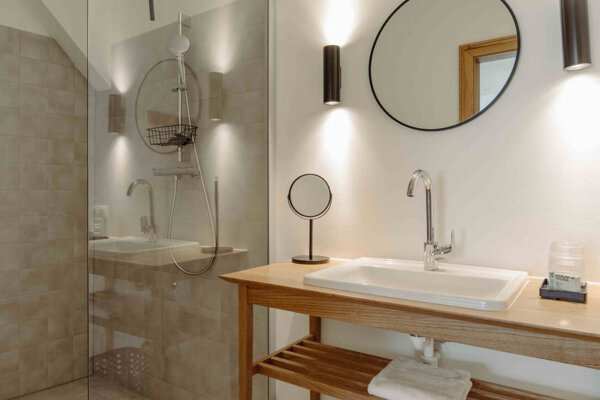 Modern bathroom with a glass shower, wooden vanity, round mirror, and soft lighting.