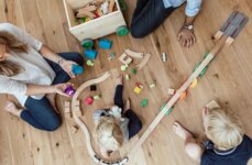 Familie spielt auf dem Holzboden mit Holzspielzeug.