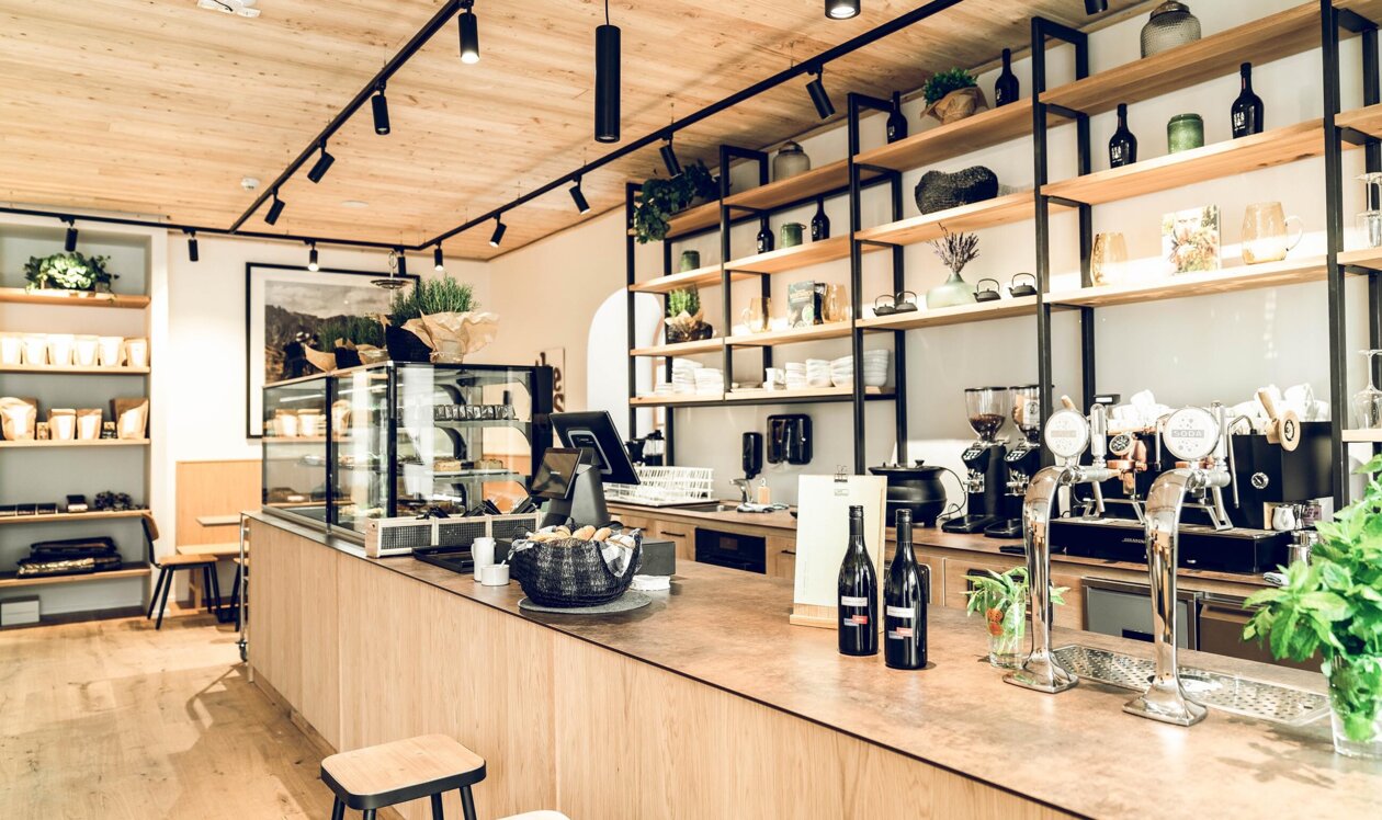 Modern café counter at Die Salzkrämerei in Hallein with espresso machines, taps, wine bottles and pastry display on warm wood shelves.