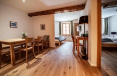 Apartment mit Wohnbereich und zwei Schlafzimmern mit Holzboden, Esstisch, Stühlen und einem Schreibtisch.