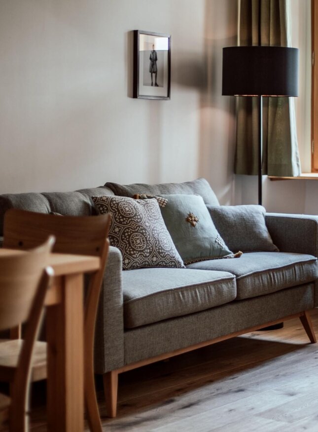 Gemütlicher Wohnbereich mit grauem Sofa, Holztisch, und großen Fenstern.