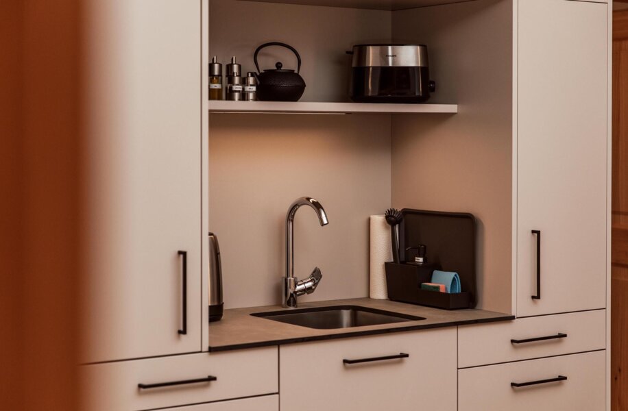 Modern kitchenette with sink, kettle, and toaster, featuring sleek cabinetry and minimalistic decor.