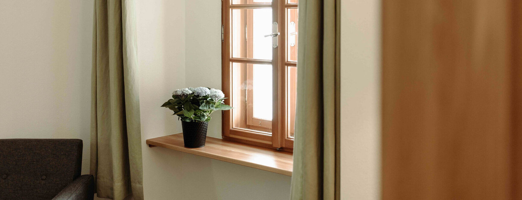Holzfenster mit beigefarbenen Vorhängen, Topfpflanze auf der Fensterbank, gemütliche Atmosphäre.