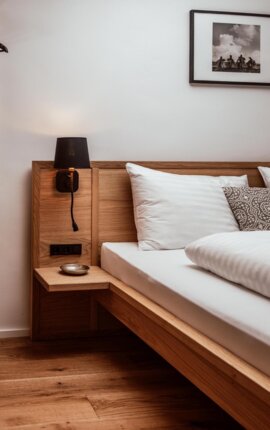 Holzbett in stilvoll gestaltetem Zimmer mit Nachttisch, Lampe und Bild an der Wand.