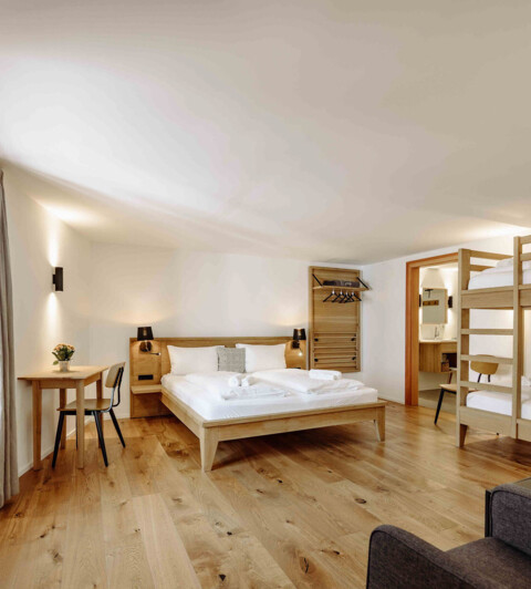 Spacious hotel room with a double bed, bunk beds, wooden flooring, and modern decor.