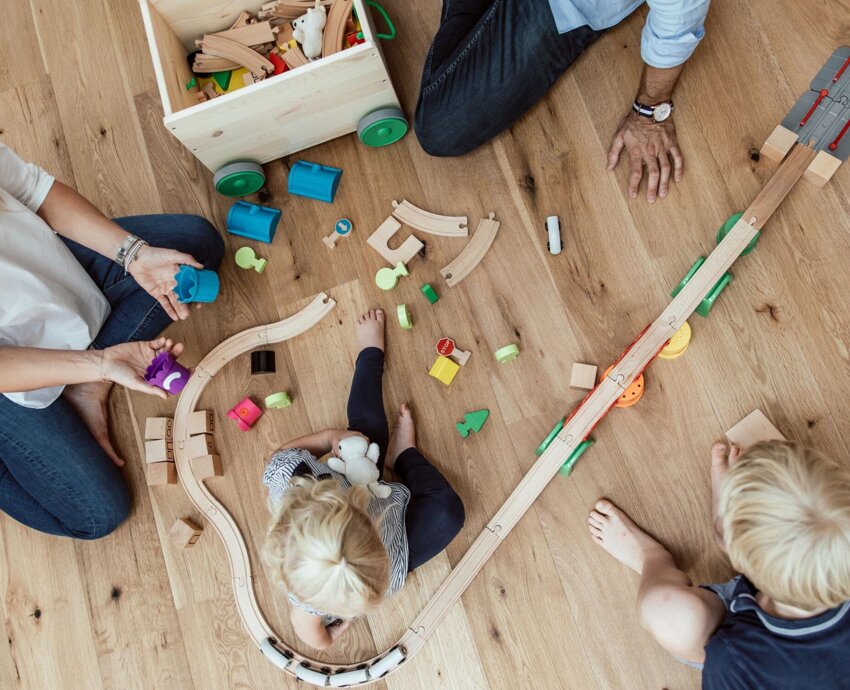 Familie spielt auf dem Holzboden mit Holzspielzeug.
