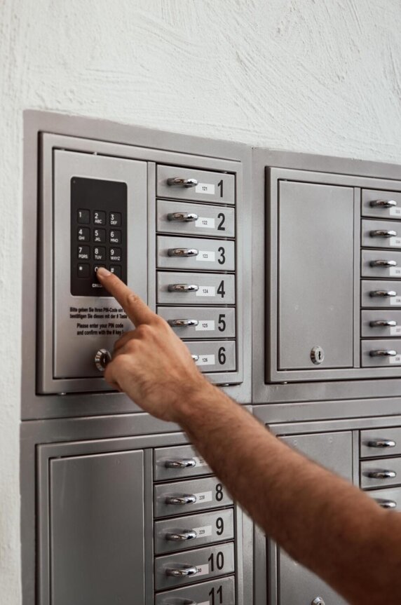 A person entering a code on a digital lock panel next to multiple numbered lockers on a wall.