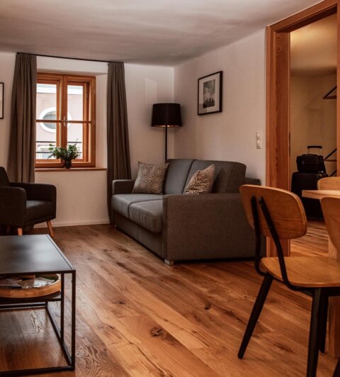 Gemütliches Wohnzimmer in einem stilvollen Apartment bei The Salt Hallein, mit Holzboden, Sofa, Tisch und Stühlen.