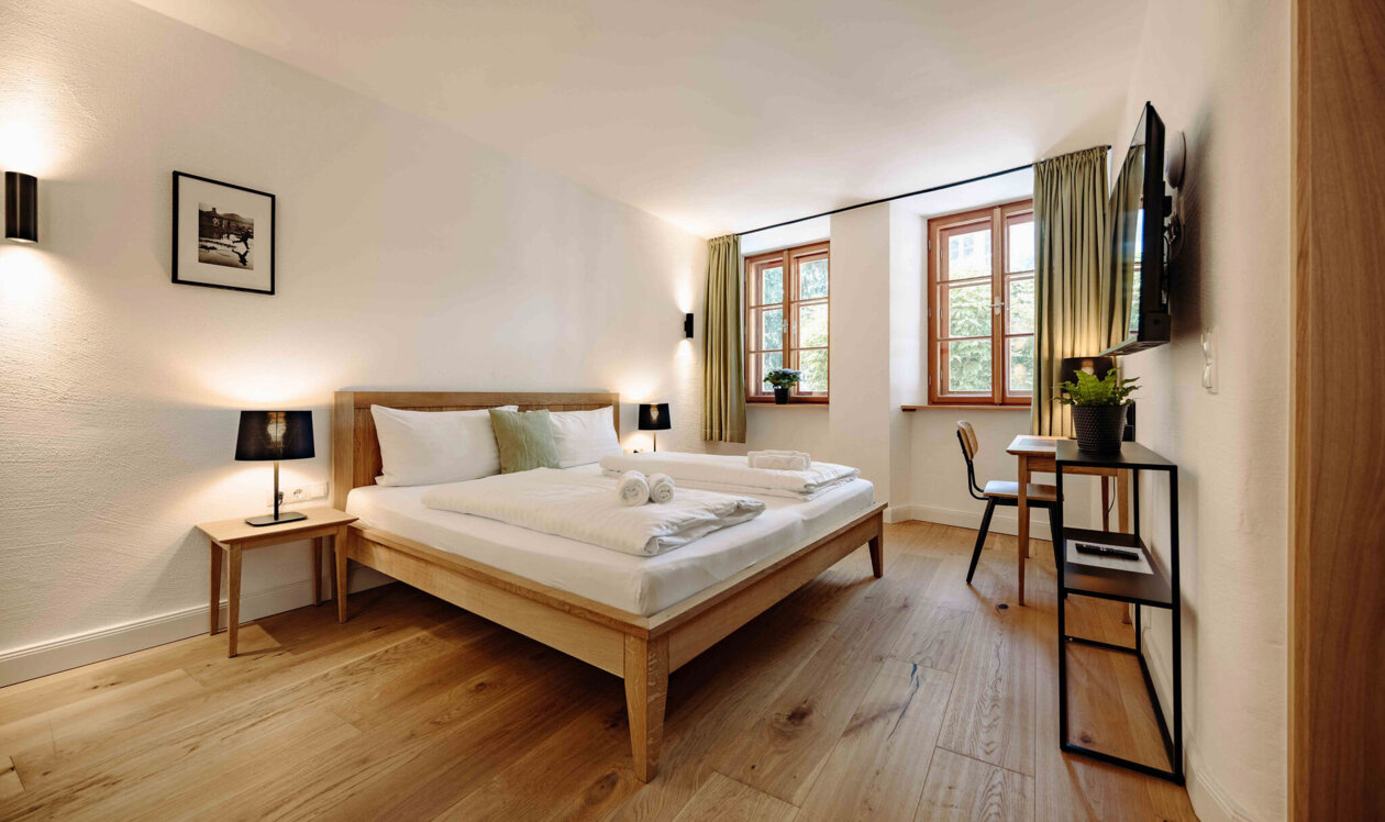 Gemütliches Schlafzimmer in stilvollem Apartment mit Doppelbett, Holzboden, TV und Schreibtisch.