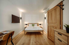 Modernes Zimmer mit Holzboden, Bett, Wand-TV, Schreibtisch und Pflanzen.
