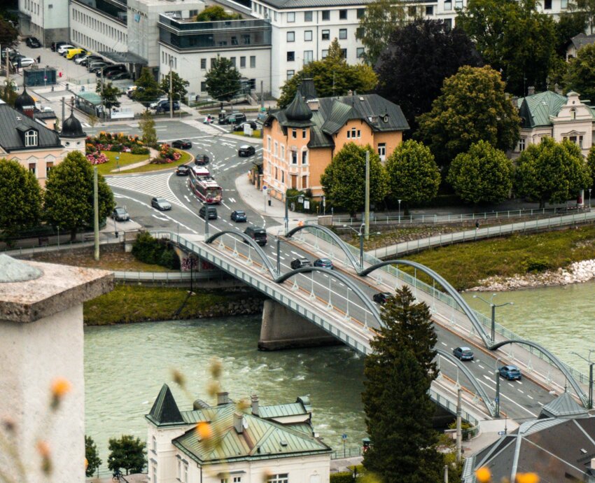Stadtansicht von Salzburg mit Brücke über der Salzach, umgeben von historischen Gebäuden und grüner Landschaft.
