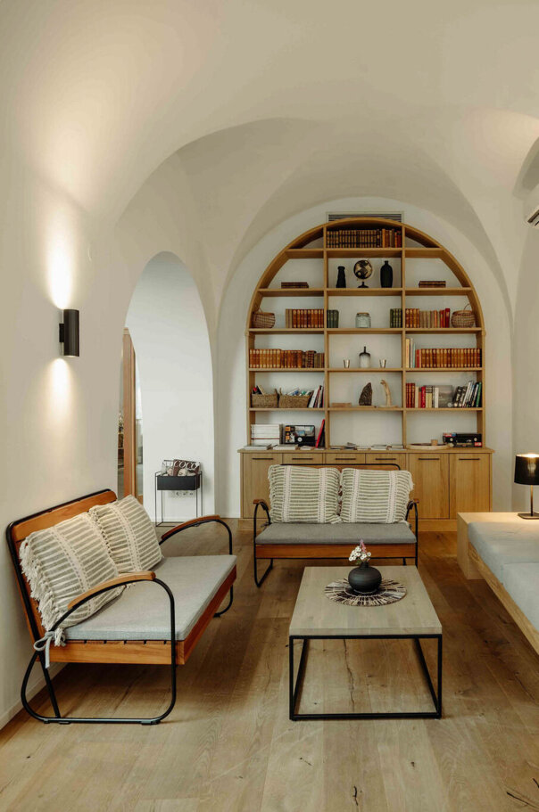 A cozy, well-lit living room with modern furniture, arched ceiling, and a bookshelf.