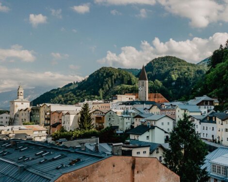 Stadtansicht von Hallein, umgeben von grünen Hügeln und einer Kirche mit Uhrturm im Zentrum unter blauem Himmel.