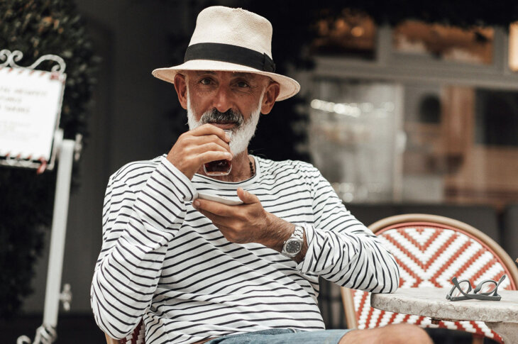 Ein Mann sitzt in einem Café, trägt einen Hut und genießt ein Getränk.