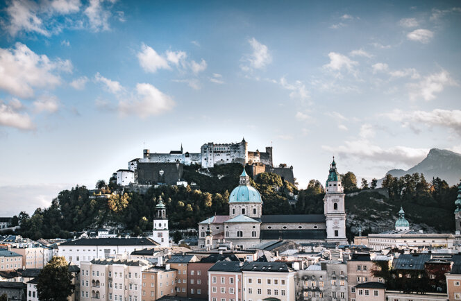 Stadtansicht von Salzburg mit Festung Hohensalzburg im Hintergrund, umgeben von historischen Gebäuden unter blauem Himmel.
