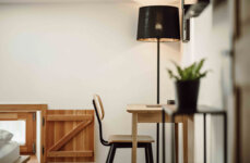 Gemütlicher Arbeitsplatz in einem stilvollen Zimmer von the salt Hallein, mit Holzstuhl, Schreibtisch, Lampe und Pflanze.