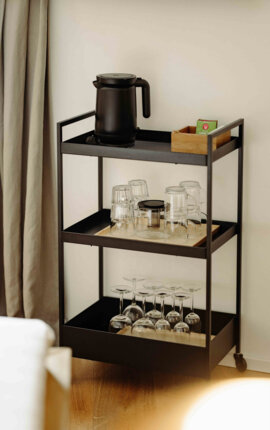 Ein schwarzer Servierwagen mit Wasserkocher, Teebox und Gläsern steht im Zimmer im the Salt in Hallein.