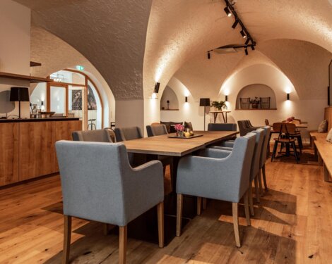 Veranstaltungsraum "Salzkammer" mit Holzboden, gewölbter Decke, großem Tisch und grauen Stühlen. Gemütliche Beleuchtung und Dekoration.