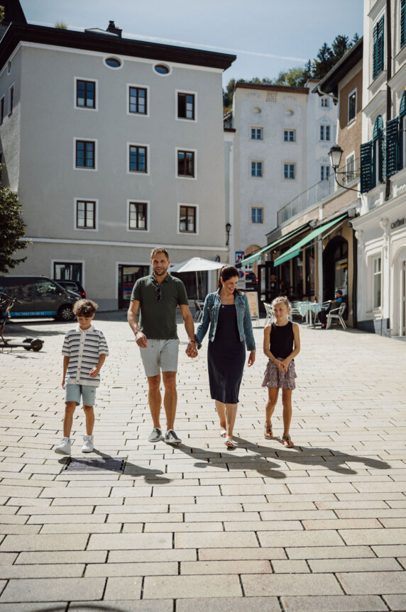 Family strolling through Hallein’s old town on a sunny day, walking past cafés and historic townhouses.