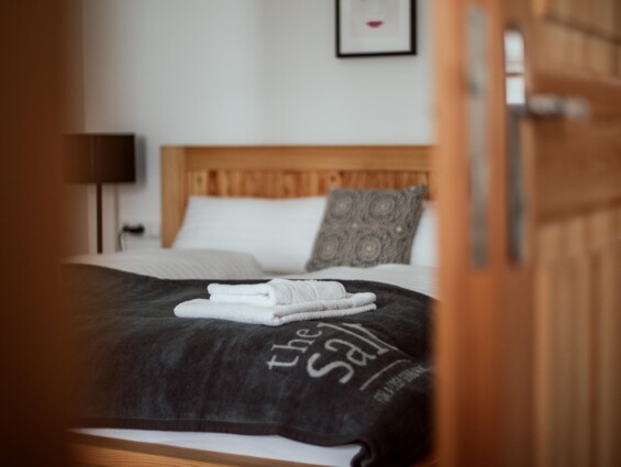 Blick in ein gemütliches Schlafzimmer mit einem Holzrahmenbett, frischen Handtüchern und stilvollem Dekor.