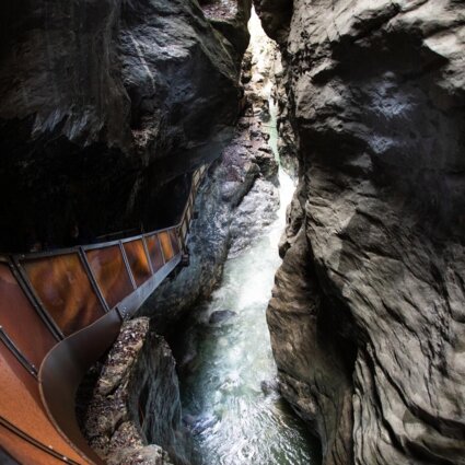 Schmaler Pfad entlang einer tiefen, felsigen Schlucht mit fließendem Wasser darunter.