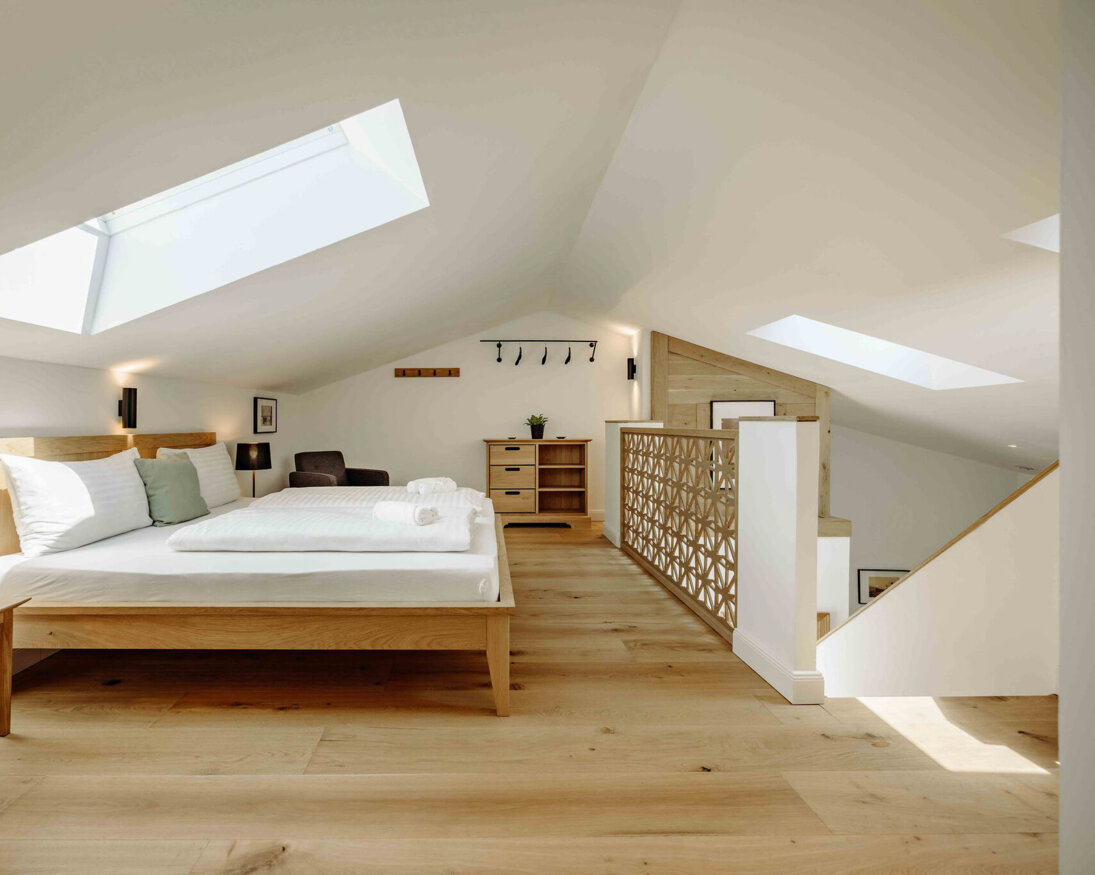 Bright attic bedroom with large skylight, wooden flooring, and minimalist decor. Cozy atmosphere with a bed, nightstand, and armchair.