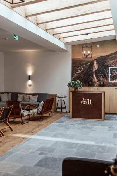 Modern hotel lobby with a wooden ceiling, cozy seating area, and a reception desk labeled "the salt." 
