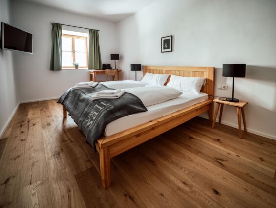 Großzügiges Schlafzimmer mit Holzboden, Doppelbett, TV und natürlichem Licht durch ein Fenster.