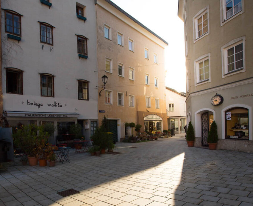 Ein sonniger Platz in Hallein, umgeben von traditionellen Gebäuden mit Geschäften und italienischem Restaurant.