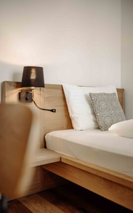 Gemütliches Schlafzimmer mit Holzbettrahmen, dekorativem Kissen und Wandlampe.