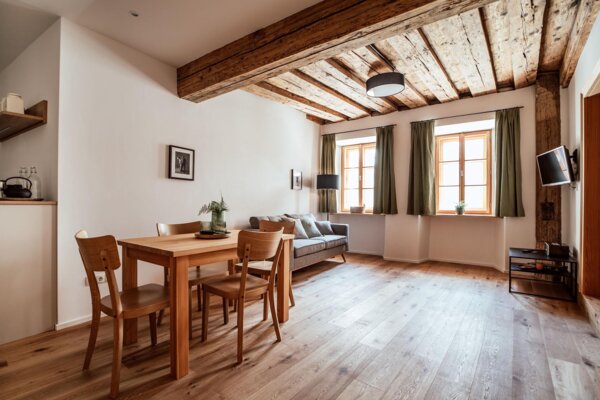 Sitzbereich im Apartment mit Holzbalkendecke, Esstisch, Sofa und hellem Holzboden in Hallein bei Salzburg.