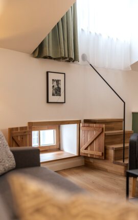 Gemütlicher Wohnbereich in einer stilvollen Ferienwohnung mit kleinem Fenster, Holzdetails und Treppe.