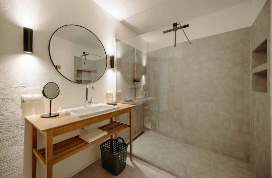 Modernes Badezimmer mit großer Dusche, Holzwaschtisch und rundem Spiegel.