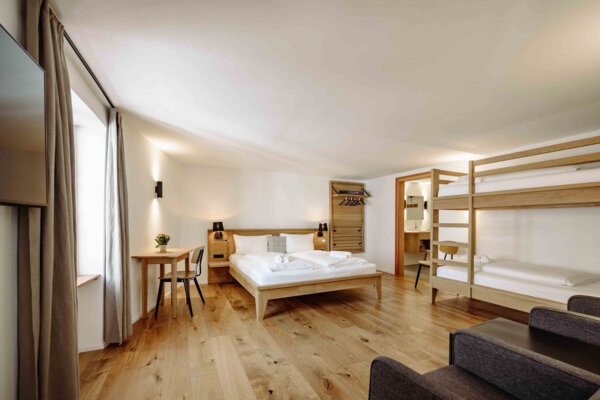Spacious hotel room with a double bed, bunk beds, wooden flooring, and modern decor.