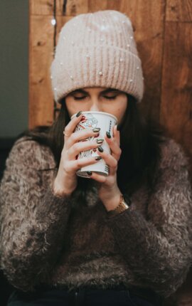 Person mit Wollhaube genießt ein Heißgetränk in gemütlicher Atmosphäre.
