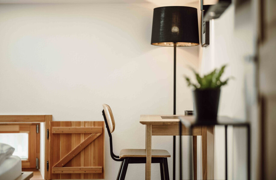 Gemütlicher Arbeitsplatz in einem stilvollen Zimmer von the salt Hallein, mit Holzstuhl, Schreibtisch, Lampe und Pflanze.