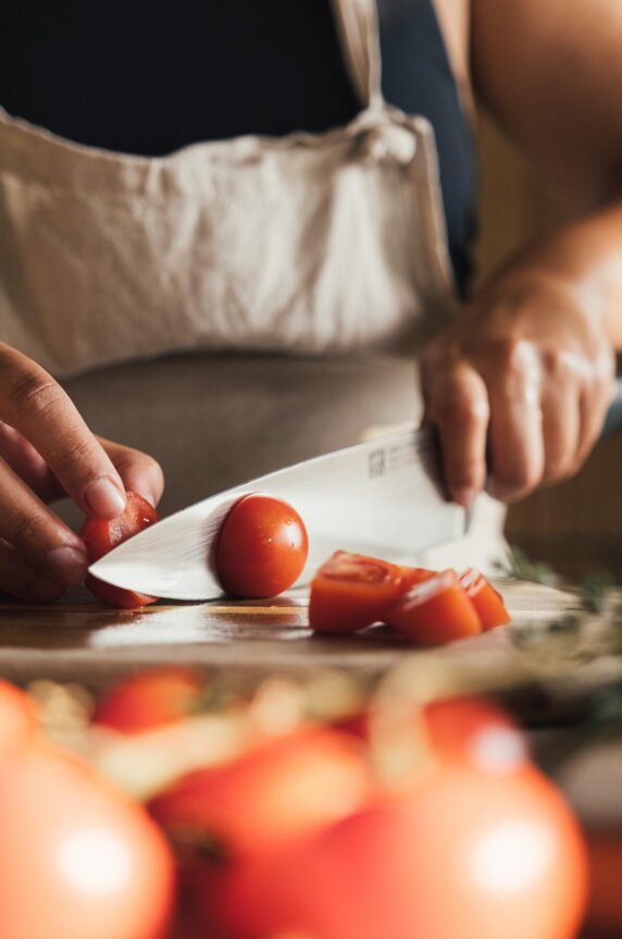 Eine Person mit Schürze schneidet frische Paradeiser auf einem Schneidebrett.