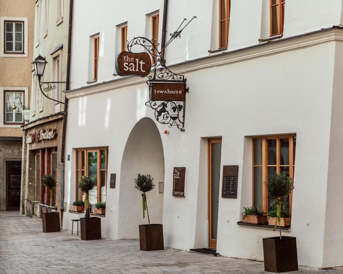 The salt townhouse exterior with potted plants, wooden windows, and decorative signage on a charming street.