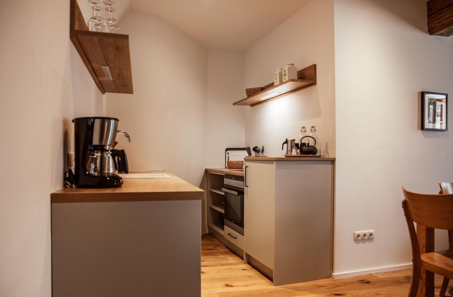 Voll ausgestattete Küche mit Kaffeemaschine, Ofen und Holzregalen in einem the salt-Apartment.