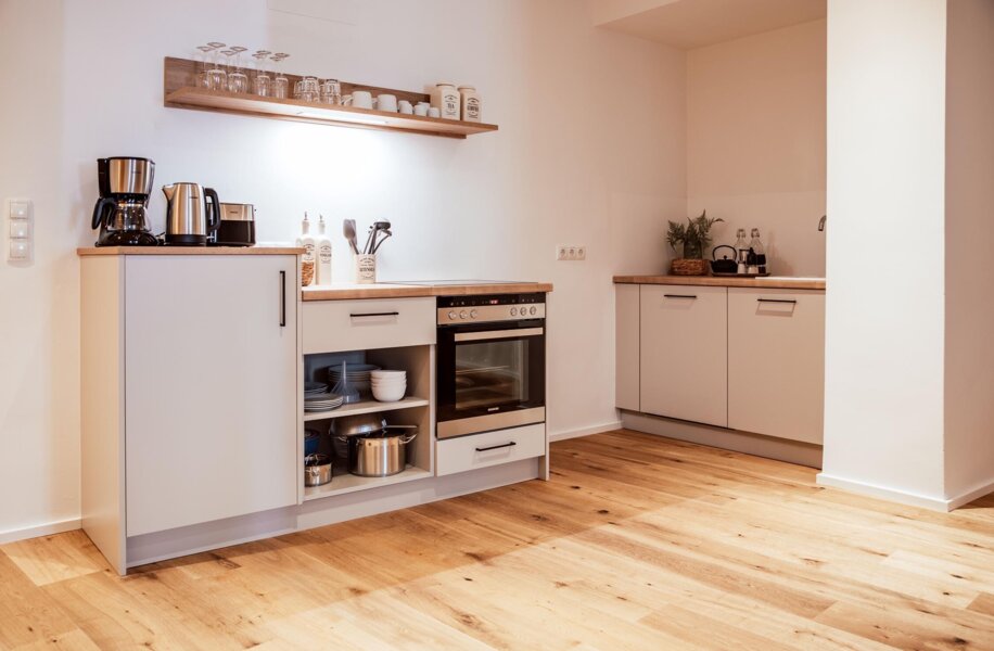 Moderne Küche mit Holzfußboden, Schränken, Ofen, Kaffeemaschine und Regal mit Geschirr.