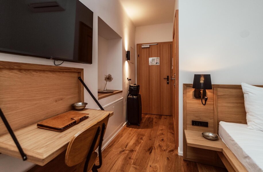 Gemütliches Hotelzimmer mit Holzinterieur, Schreibtisch, Fernseher und Koffer. Elegantes Ambiente und warme Beleuchtung.