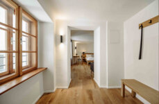 Heller Flur mit Holzboden, Fenster und Blick in ein gemütliches Zimmer im the salt Hallein.