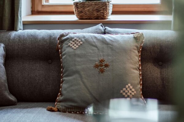 Gemütliches Wohnzimmer mit grauem Sofa und dekorativem Kissen, Pflanze auf Fensterbank.