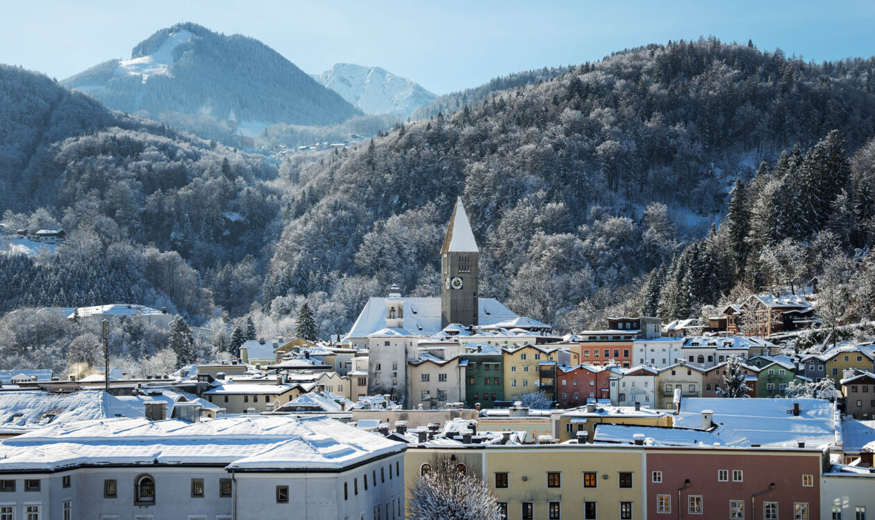 Hallein im Winter mit bunten Häusern und schneebedeckten Bergen im Hintergrund.