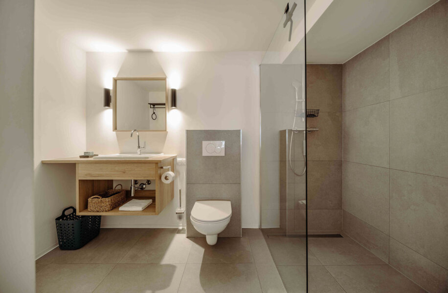 Modernes Badezimmer mit begehbarer Dusche, hölzernem Waschtisch, Spiegel und WC. Elegantes Design und klare Linien betonen den Raum.