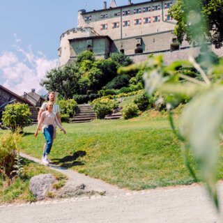 Ein Paar spaziert durch eine grüne Landschaft mit einer Burg im Hintergrund.