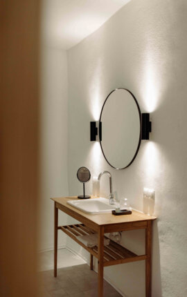 Modernes Badezimmer mit Holzwaschtisch, rundem Spiegel und eleganter Beleuchtung.
