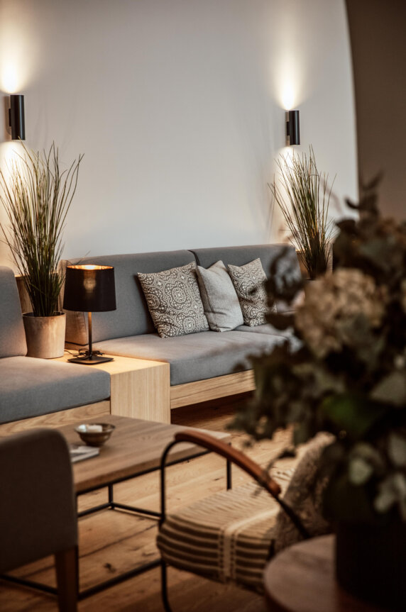 Moderner Sitzbereich mit grauem Sofa, dekorativen Kissen und Pflanzen. Stimmungsvolle Beleuchtung ergänzt das gemütliche Ambiente.